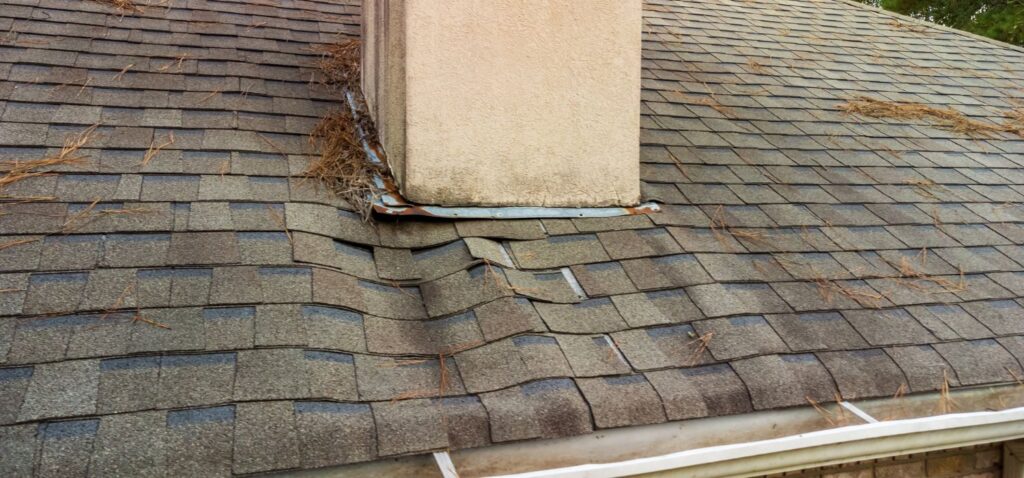 A close-up view of a roof with water-damaged shingles and debris around a chimney, showing signs of wear and potential water leakage.